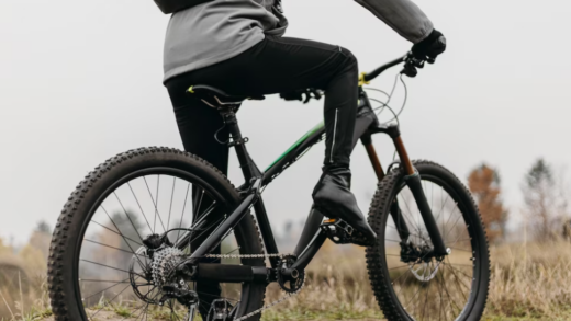 man riding a bike on the land with grass, trees on the background